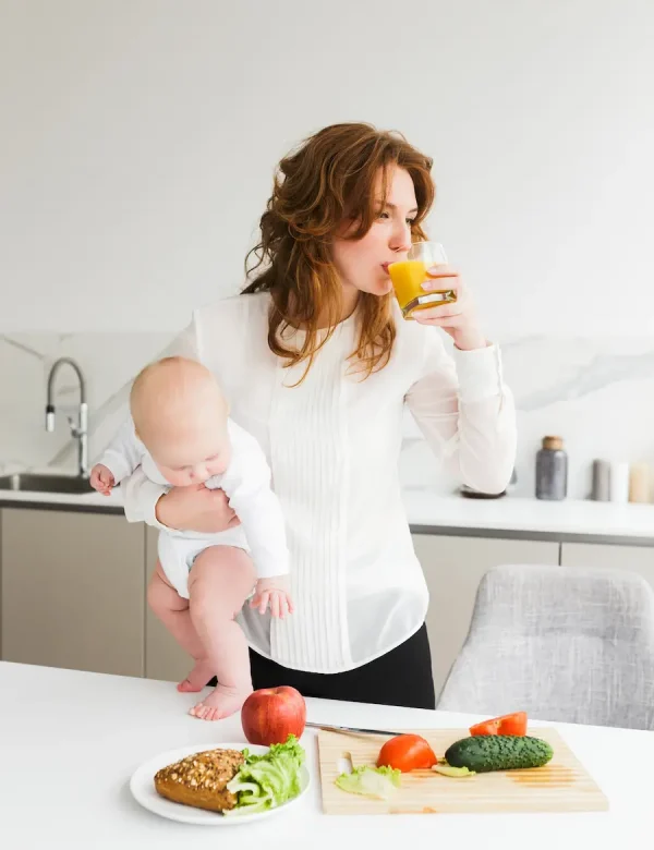 portrait-young-pretty-woman-standing-holding-her-little-baby-while-drinking-juice-cooking-kitchen